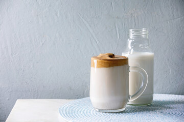 Dalgona frothy coffee trend korean drink milk latte with coffee foam in glass mug, bottle of milk on white marble table. Copy space
