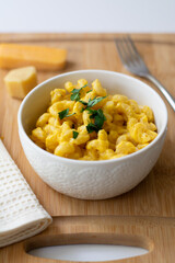 Traditional American macaroni and cheese comfort food (also called mac n cheese) with elbow pasta coated in a cheesy creamy cheddar sauce. Topped with parsley, cheese in the background.
