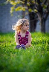 Beautiful child girl blonde walks in the summer in the sun in the green grass