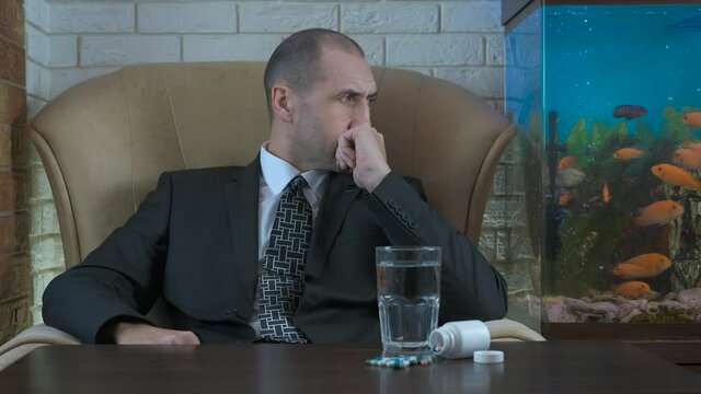 Businessman and antidepressants. Pensive man in a business suit with pills on the table.