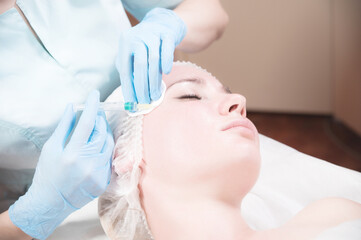 Naklejka premium A female beautician makes an injection to a female client in a cosmetics office. Cosmetic procedures for rejuvenation