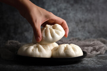 Close up hand holding a steamed pork bun, Chinese dim sum cuisine.