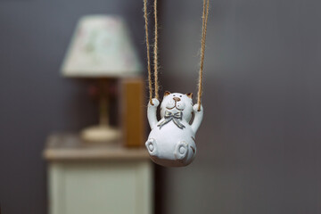 white clay figurine of a cat swinging on a thread, in the background a night lamp.
lmage with...