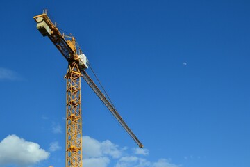 Fototapeta na wymiar One industrial crane against blue sky. Small moon included. Construction site. Construction crane tower on blue sky background. Empty Space for text. Construction concept.