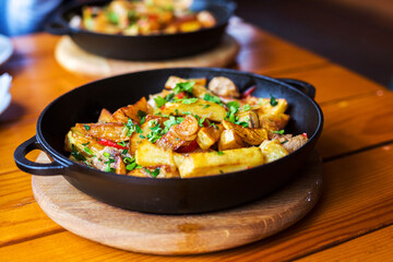 Authentic fried potatoes with bacon and parsley on black pan. Morning atmospheric lighting, fashionable trendy spot soft focus. Preparation for design creative menu.