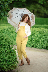 Young pregnant woman under umbrella in summer forest.