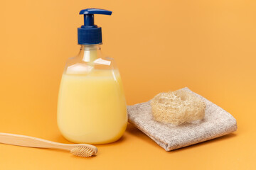 Bottle of liquid soap yellow and bamboo toothbrushes with a sponge made of natural material on a beige background. Clean hands concept. Shampoo, Liquid Soap, Aromatic Bath Salt And Other Toiletry.