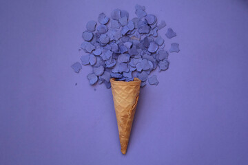 Top view of ice cream cone with purple confetti on purple background