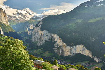 Fototapeta premium Lauterbrunnen Valley at sunset with snowy mountains, waterfall and green nature. Landscape panorama taken from mountain village Wengen, Switzerland