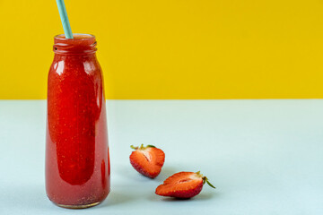 Strawberry smoothie in a glass bottle. Berry summer cocktail on a pastel background. Fruit minimal concept. Close-up, copy space