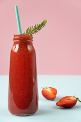 Strawberry smoothie in a glass bottle. Berry summer cocktail on a pastel background. Fruit minimal concept. Close-up, vertical