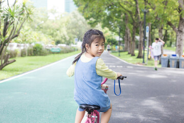 Portrait of little asian girl on a bicycle in summer city park outdoors