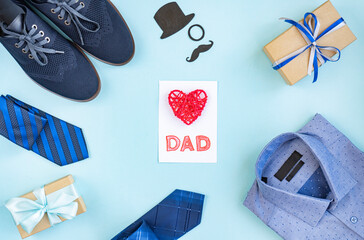 Background of father's Day. A gift box, shoes, tie, shirt, and holiday decoration on a light blue table. Top view, flat lay, copy space