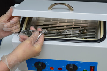 gloved hand with forceps for manicure, a hot air sterilizer, preparation of tools for steam...