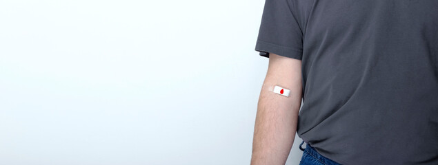 Blood donorship. Man in gray T-shirt hand taped with patch with red drop after giving blood on gray...
