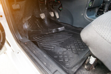 Open driver's door close-up of dirty rubber rug under the feet with gas, brake and clutch pedals in...