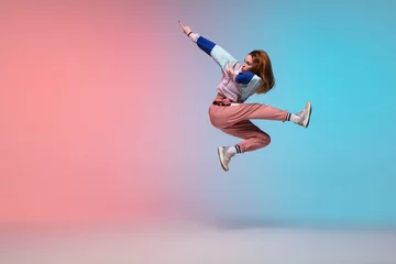 Fotobehang In jump. Beautiful girl dancing hip-hop in stylish clothes on colorful gradient background at dance hall in neon light. Youth culture, movement, style and fashion, action. Fashionable bright portrait. © master1305