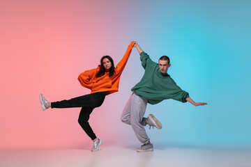 Boy and girl dancing hip-hop in stylish clothes on colorful gradient background at dance hall in...