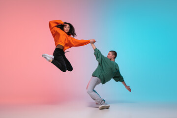 In jump. Boy and girl dancing hip-hop in stylish clothes on colorful gradient background at dance hall in neon. Youth culture, movement, style and fashion, action. Fashionable portrait. Street dance.
