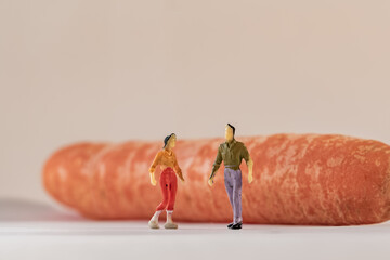 Miniature woman and man figure standing next to big orange carrot. Shallow depth of field background. Healthcare, healthy lifestyles and slimming concept.