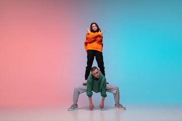 Fototapeta na wymiar Boy and girl dancing hip-hop in stylish clothes on colorful gradient background at dance hall in neon. Youth culture, movement, style and fashion, action. Fashionable bright portrait. Street dance.