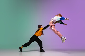 Beautiful sportive girls dancing hip-hop in stylish clothes on colorful gradient background at...