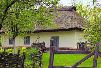 Fototapeta na wymiar Close-up view of small ancient clay house with a garden surrounded by a wicker fence in sunny day. Concept of historical buildings of ancient Ukraine
