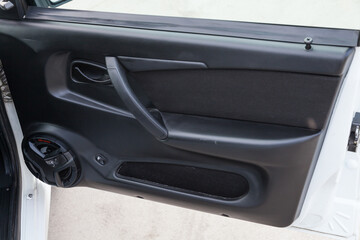Close-up of the open front door of a Russian LADA vaz 2114 car with a new factory-made music speaker on a black plastic panel, next to the power window buttons, a handle and a storage compartment.