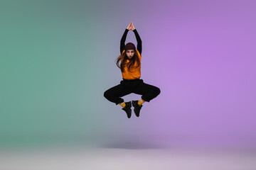 In jump. Beautiful girl dancing hip-hop in stylish clothes on colorful gradient background at dance hall in neon light. Youth culture, movement, style and fashion, action. Fashionable bright portrait.