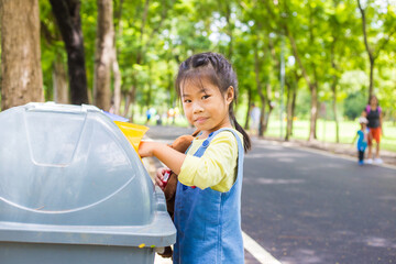 Adorable little girl keep park clean throw trash into plastic bin