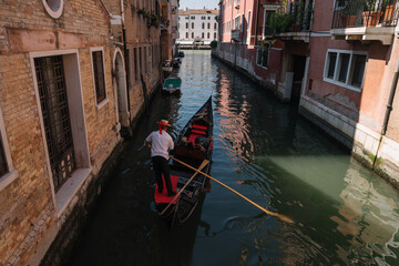 Fototapeta na wymiar Gondolier drives a gondola with two tourists on a canal in Venice, Italy.