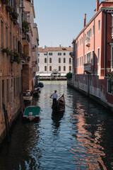 Gondolier drives a gondola with tourists on a canal in Venice, Italy.