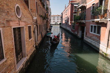 Gondolier drives a gondola with two tourists on a canal in Venice, Italy.
