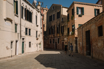 Fototapeta na wymiar Tourists are walking along the narrow and bright streets of sunny Venice, Italy.