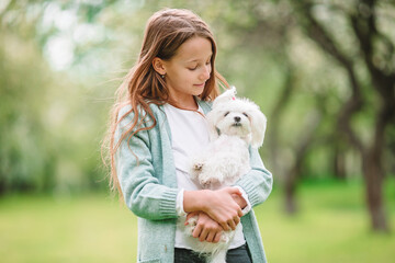 Little smiling girl playing and hugging puppy in the park