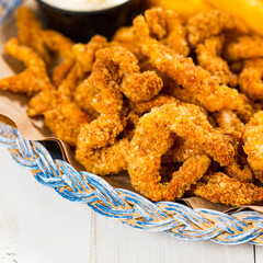 Crispy Breaded Clam Strips Snack Size. Deep Fried Breaded Clams Fingers and French Fried Potatoes with Tartar Dipping Sauce on a wooden board. Selective focus.