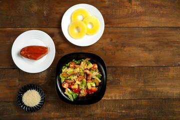 Pan-Asian salad with cherry tomatoes, smoked chicken, pineapple and sesame seeds in a black plate...