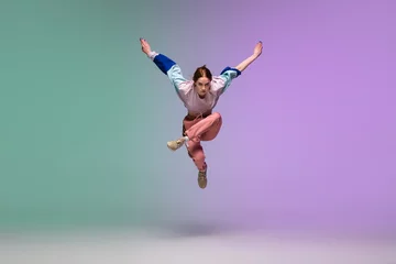Foto op Plexiglas In jump. Beautiful girl dancing hip-hop in stylish clothes on colorful gradient background at dance hall in neon light. Youth culture, movement, style and fashion, action. Fashionable bright portrait. © master1305