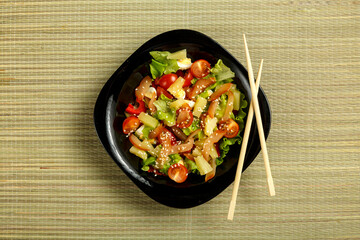 Pan-Asian salad with chicken and pineapple in a black plate on a bamboo mat and chopsticks.