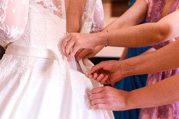 Bridesmaids hands helping bride to get her wedding dress on