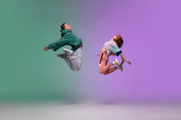 High jump. Boy and girl dancing hip-hop in stylish clothes on colorful gradient background at dance...