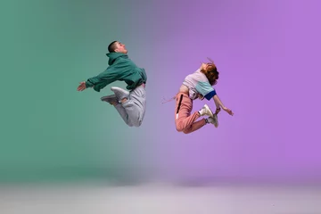 Foto op Canvas High jump. Boy and girl dancing hip-hop in stylish clothes on colorful gradient background at dance hall in neon. Youth culture, movement, style and fashion, action. Fashionable portrait. Street dance © master1305