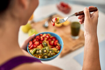 Close-up of woman eating fruit salad in the kitchen.