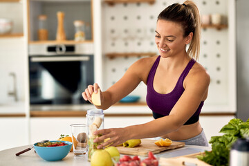 Young athletic woman making fruit smoothie in the kitchen.