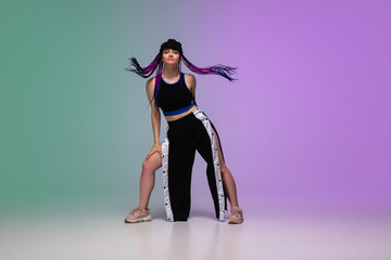 Beautiful sportive girl dancing hip-hop in stylish clothes on colorful gradient background at dance hall in neon light. Youth culture, movement, style and fashion, action. Fashionable bright portrait.