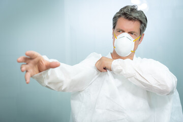 Male caucasian doctor wearing mask puts on white gown.