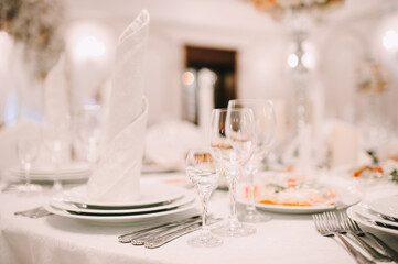 Banquet, restaurant. Table setting with tablecloth. White plates, cutlery, glasses, napkin, floral arrangements, food, chairs, flowers