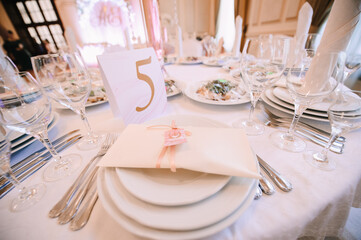 Banquet, restaurant. Table setting with tablecloth. White plates, cutlery, glasses, napkin, floral arrangements, food, chairs, flowers