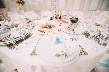 Banquet, restaurant. Table setting with tablecloth. White plates, cutlery, glasses, napkin, floral arrangements, food, chairs, flowers