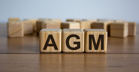 Concept word 'AGM' - acronym of words 'annual general meeting' on cubes on a beautiful wooden table. White background. Business concept.